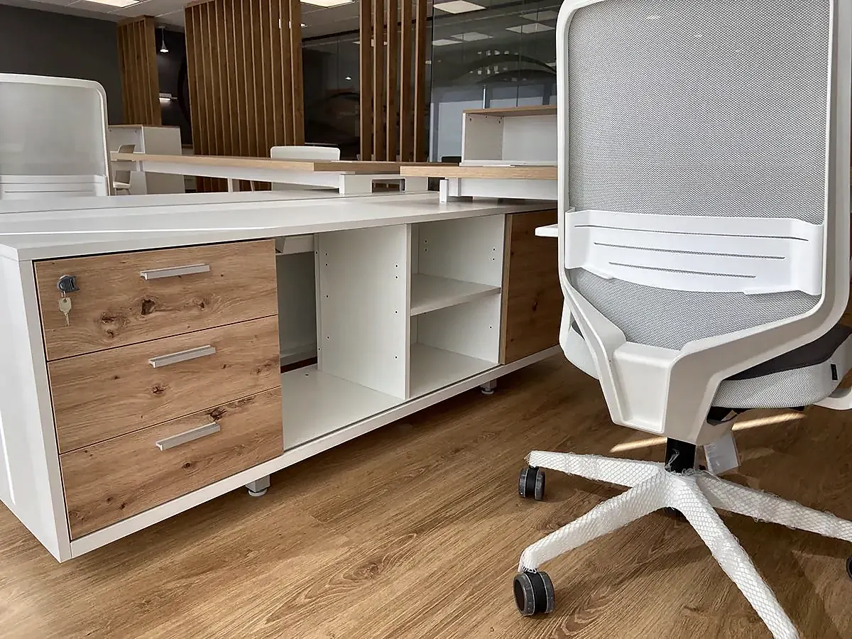Detalle de un puesto de trabajo con cajonera de madera y silla blanca