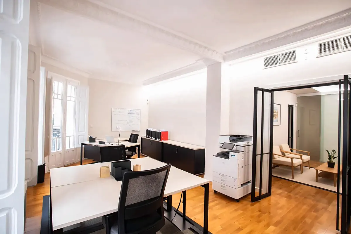 Zona de trabajo con mesa blanca, mobiliario oscuro y puertas acristaladas