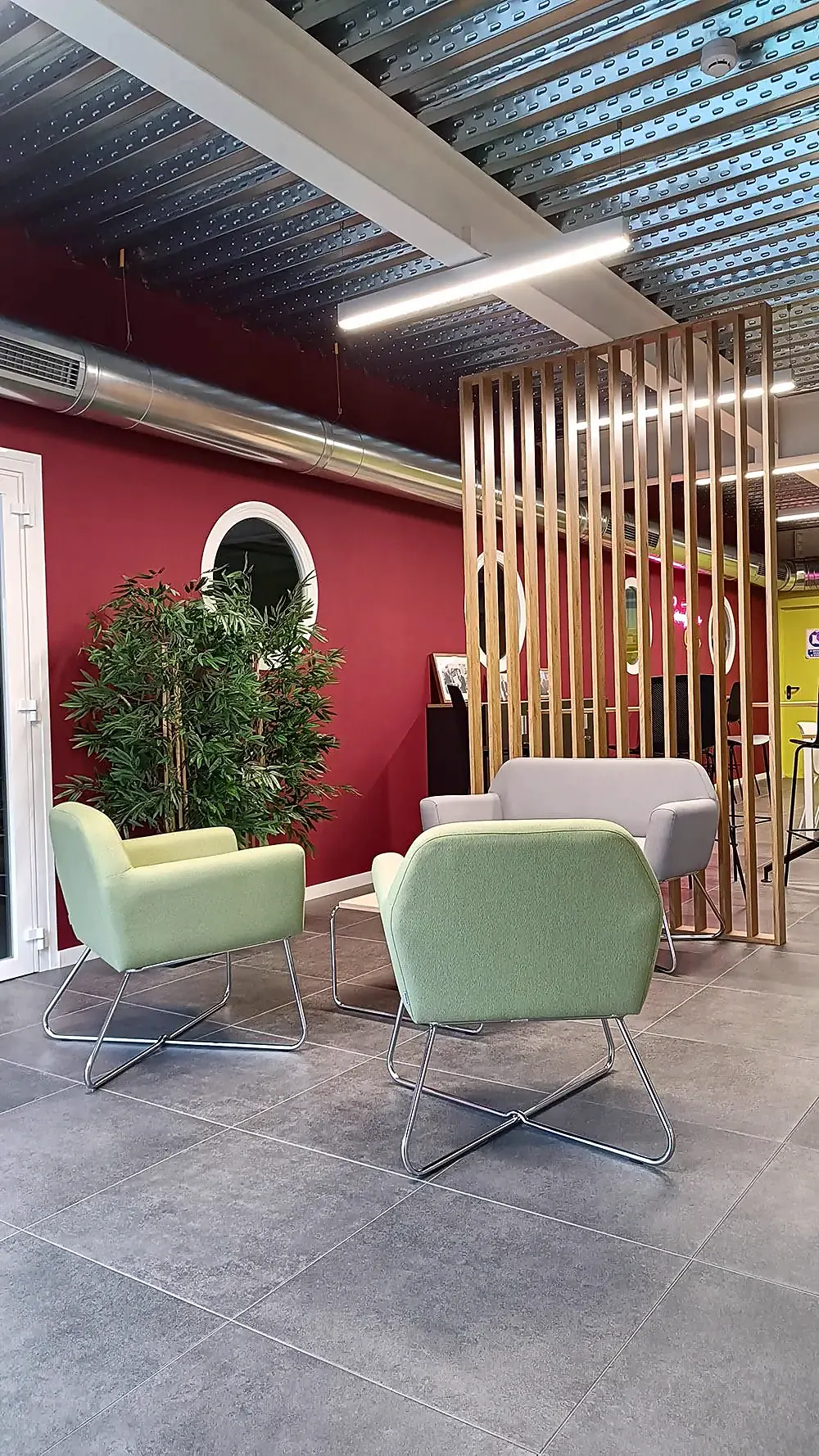 Zona social de Gripple en Zaragoza: butacas verdes junto a una celosía de lamas de madera, entre vegetación